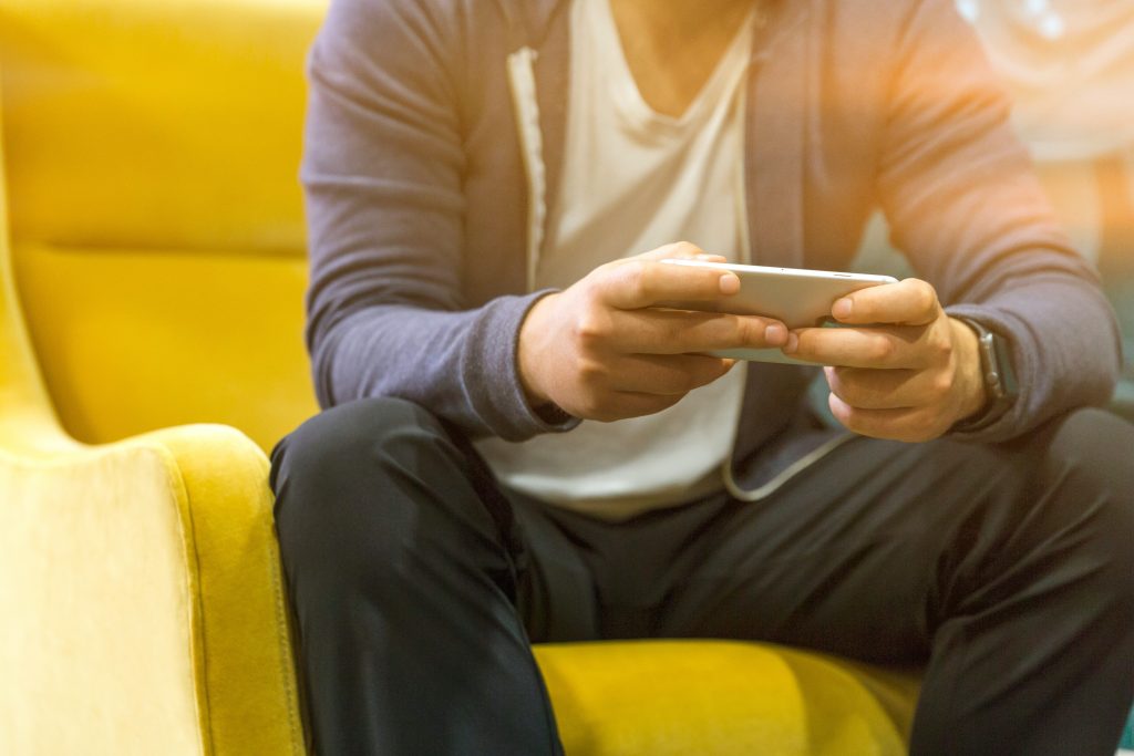 man wearing blue jacket and white shirt, sitting on couch using smartphone