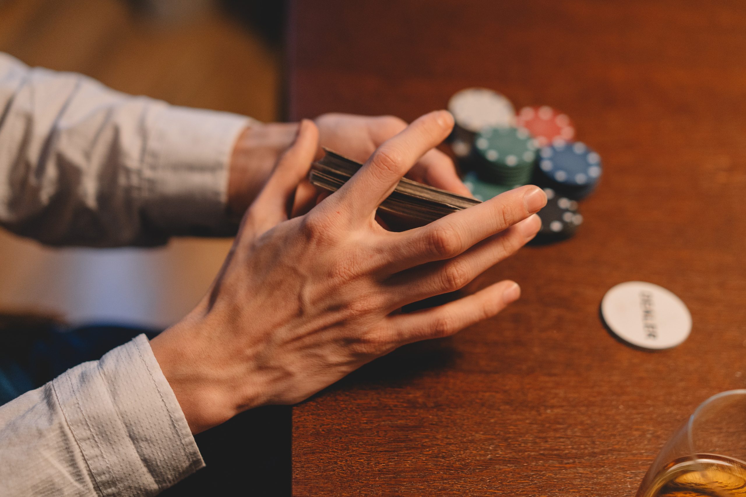 person holding playing cards with casino chips scattered on the wooden table